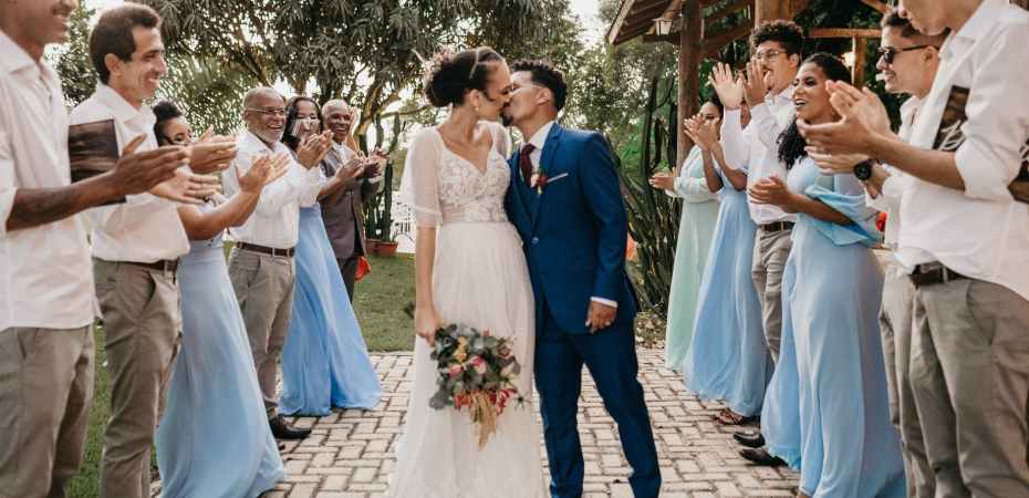multiethnic couple kissing between smiling guests on wedding day