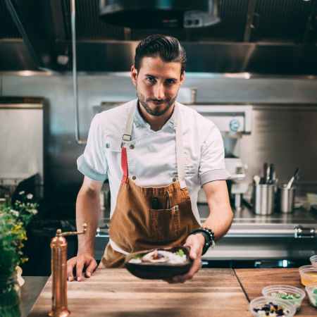 man in white chef uniform holding a brown wooden tray